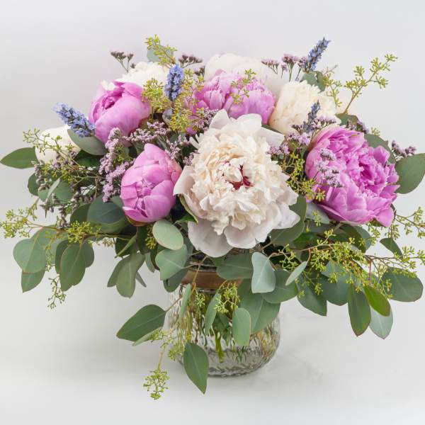 Low glass vase arrangement with pink and white blossoms and purple accents in a loose, full design