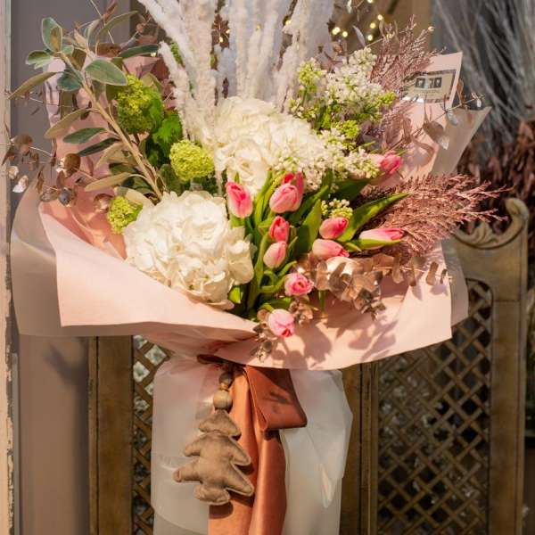 Tall bouquet of white and pink flowers wrapped in blush paper with a satin ribbon