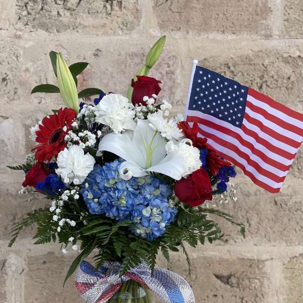Bouquet of red, white, and blue flowers in a glass vase with an American flag