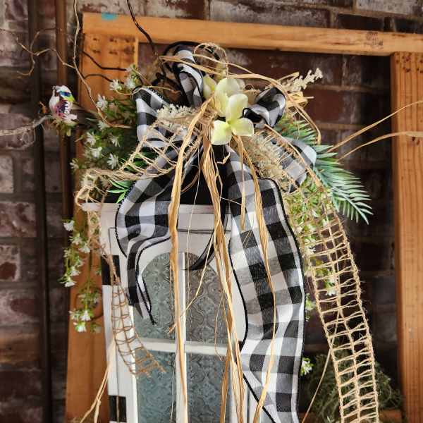 Decorative floral arrangement on a white lantern with black plaid ribbon
