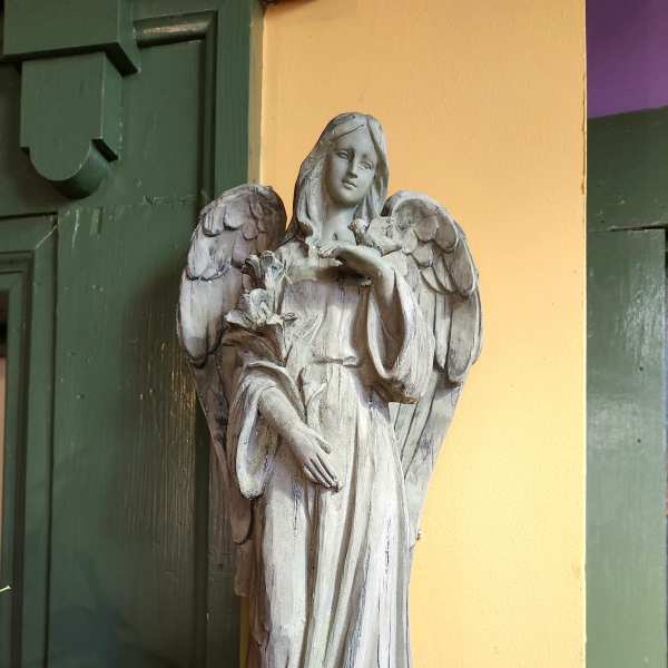 A carved angel statue holding flowers stands against a yellow wall.