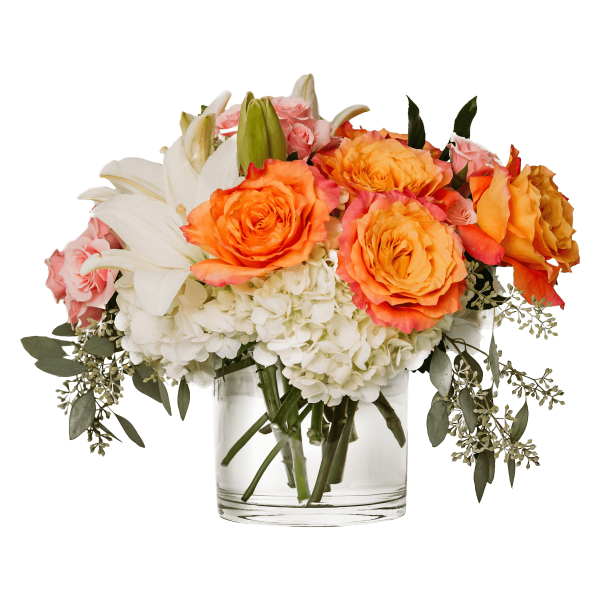 Low glass vase with orange roses, white lilies, white hydrangeas, and pink spray roses in a compact arrangement