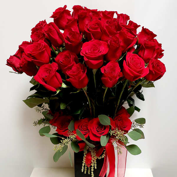 Red roses arranged in a black rectangular vase with a red ribbon