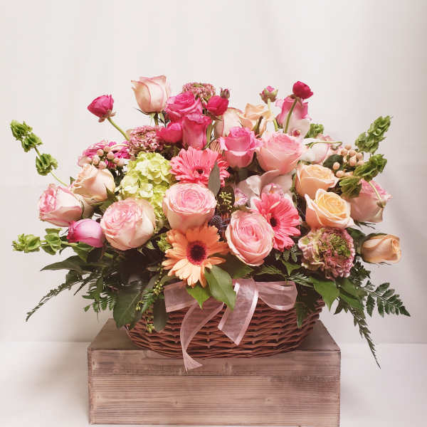 Pink and peach flower arrangement in a wicker basket with a ribbon