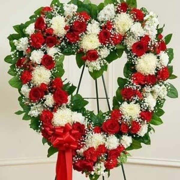 Heart-shaped wreath of red and white flowers on a stand with a red ribbon