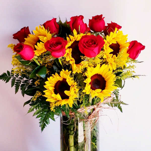 Bouquet of red roses and yellow sunflowers in a tall glass vase