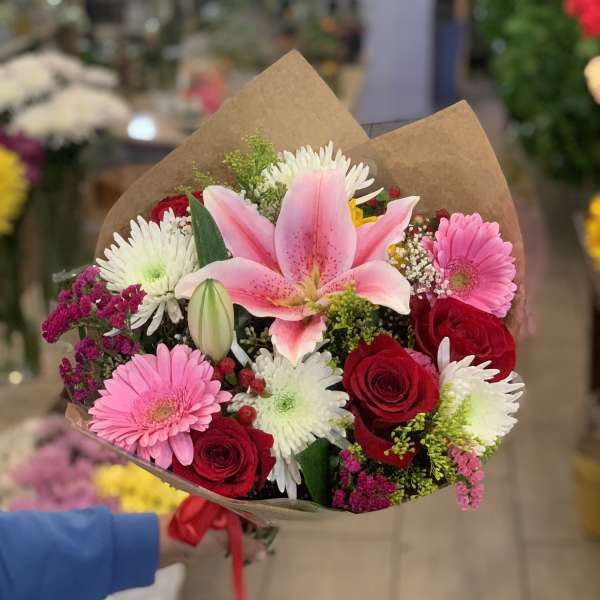 Bouquet of pink lilies, red roses, and pink and white daisies wrapped in brown paper