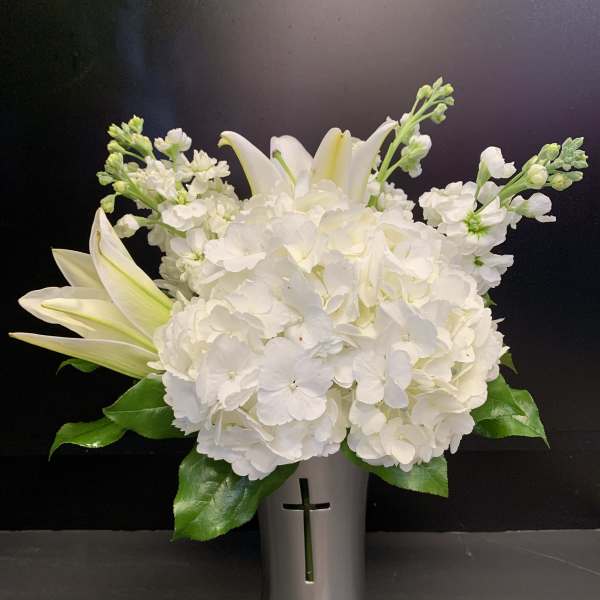 White hydrangea and lilies arranged in a silver vase with a cross cutout