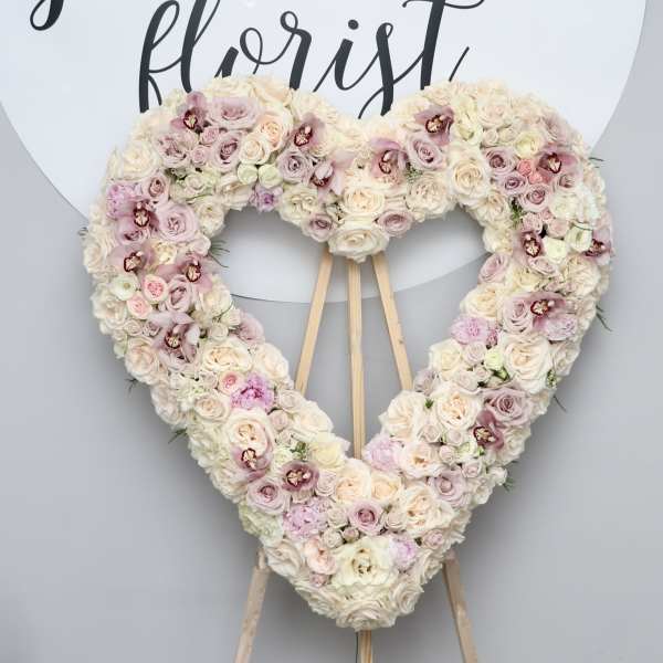 Heart-shaped floral wreath on an easel with pale pink and cream roses