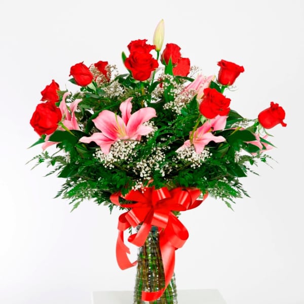 Red roses and pink lilies in a glass vase with a red ribbon