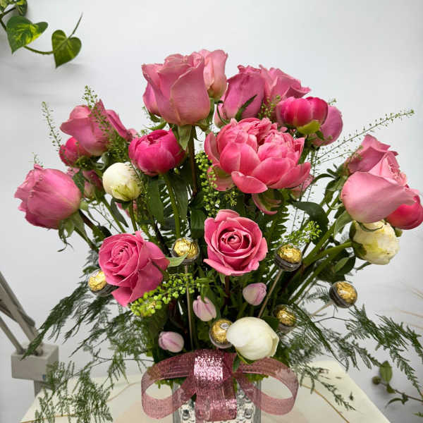 Pink roses and peonies arranged in a glass vase with a pink ribbon