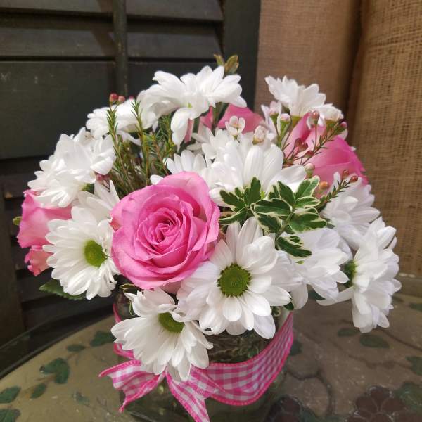 Pink roses and white daisies in a glass vase with a pink ribbon