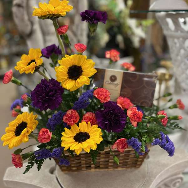 Basket arrangement with yellow sunflowers, purple carnations, and pink mini carnations