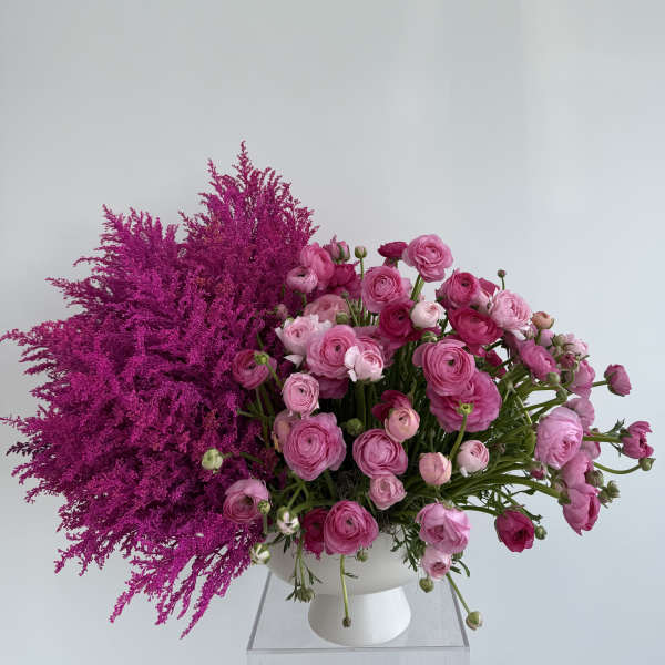 Pink ranunculus arrangement in a white vase with magenta filler