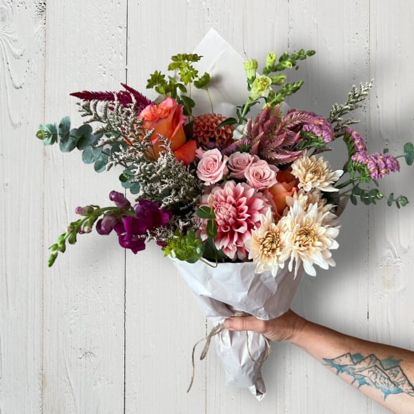 Hand-tied bouquet of pink, orange, and cream flowers wrapped in white paper