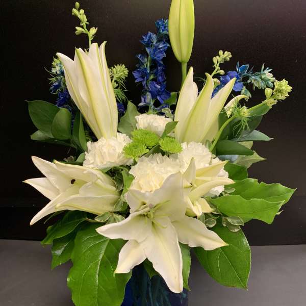 White lilies and blue flowers arranged in a blue vase