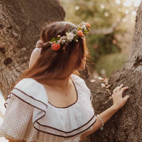 Woman wearing a floral crown and white dress standing by a tree