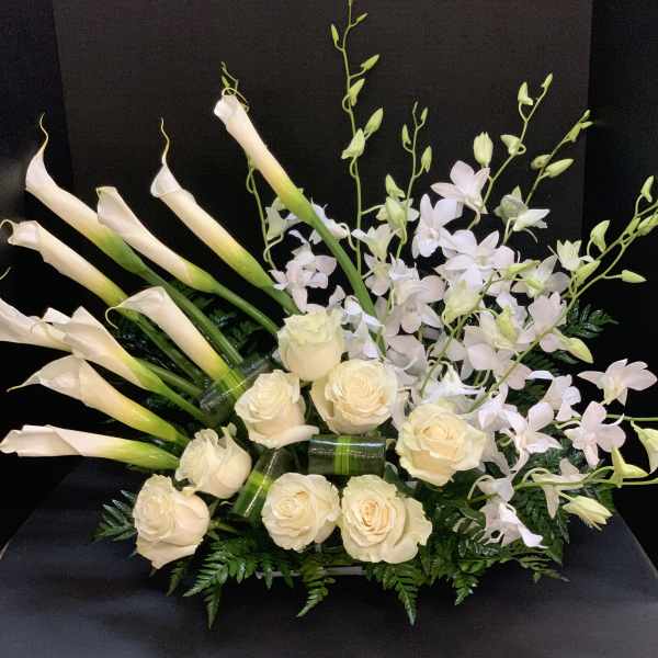 Cream calla lilies, roses, and pale orchids in a low black container