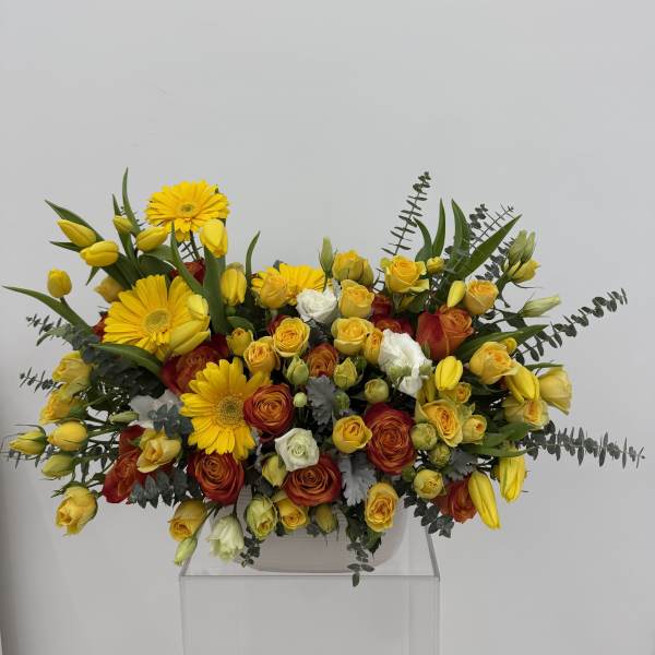 Yellow gerberas and roses arranged in a low white container
