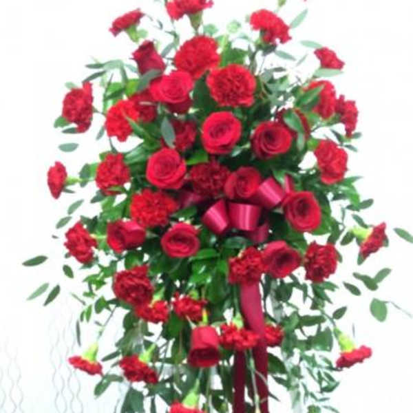 Tall standing spray of red roses and carnations with a burgundy ribbon