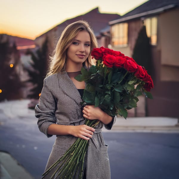 Woman holding a large bouquet of red roses outdoors at sunset