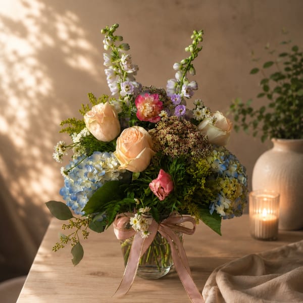 Bouquet of pastel roses, hydrangeas, and tall lavender blooms in a glass vase