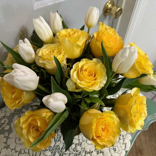 Arrangement of yellow roses and white tulips in a compact round bouquet on a lace-covered table