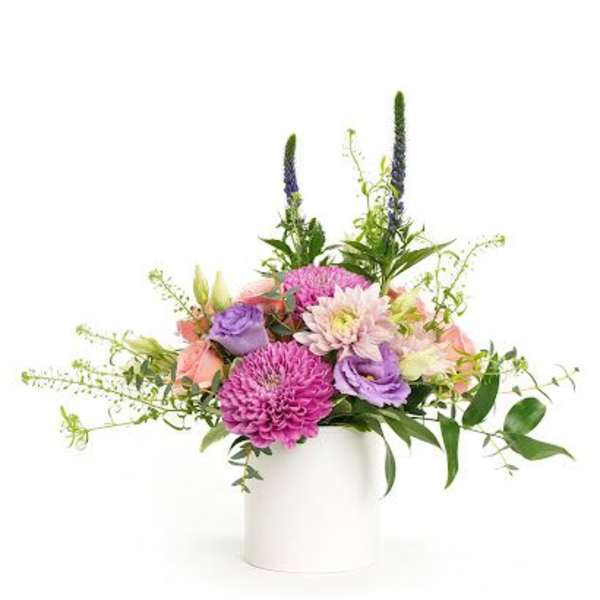 Mixed arrangement of pink and purple flowers with peach accents in a white cylinder vase