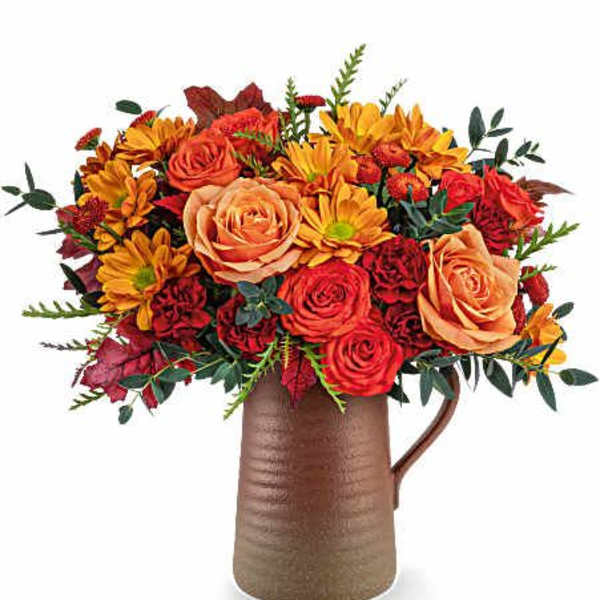 Bouquet of orange roses and yellow daisies in a brown pitcher vase
