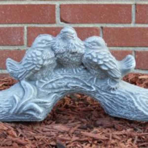 Decorative stone bird sculpture on mulch in front of a brick wall