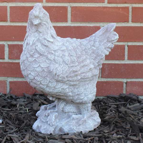 White chicken statue on mulch in front of a brick wall