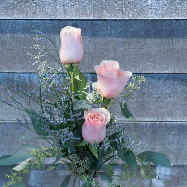 Pink roses in a clear glass vase with airy purple filler