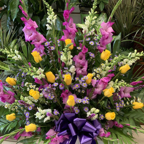 Large mixed floral arrangement in a white pedestal vase with a purple bow