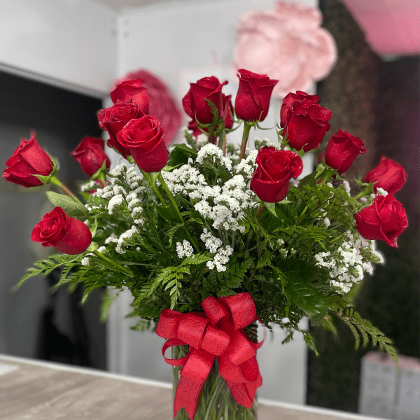 Red roses in a clear glass vase with white filler flowers and a red ribbon