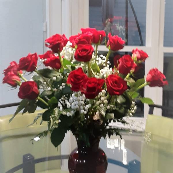 Red roses arranged in a dark glass vase with white filler flowers