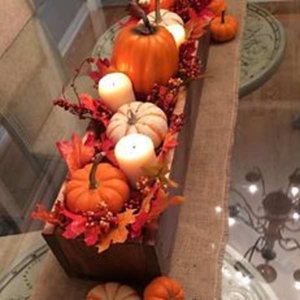 Pumpkins and white candles arranged in a long wooden tray
