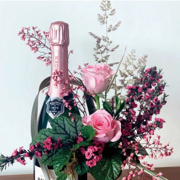 Pink roses arranged around a champagne bottle with pink filler flowers