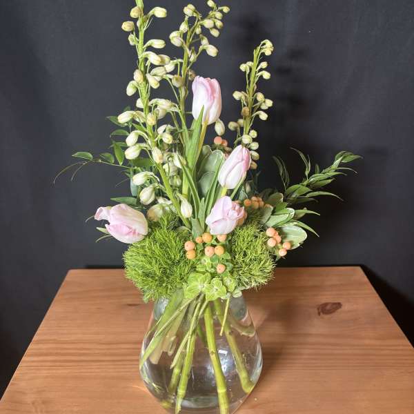 Pink tulips and green berry stems in a glass vase
