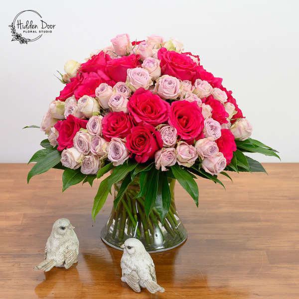 Pink and blush roses in a glass vase with two small bird figurines