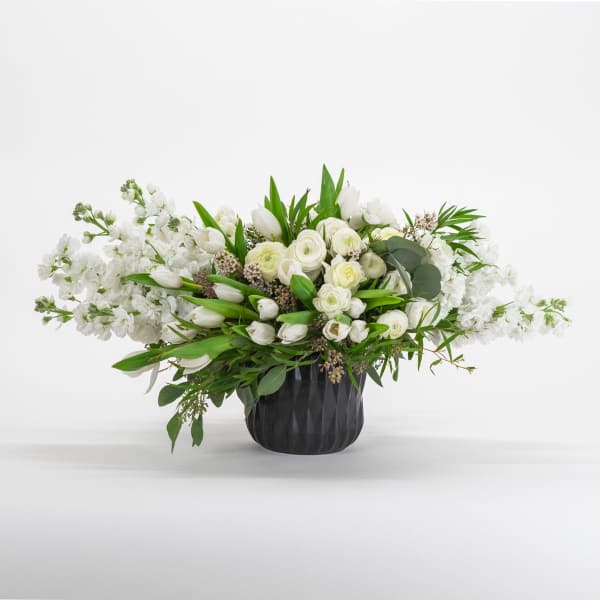 White floral arrangement in a black vase with long green foliage