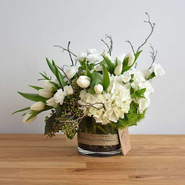 White floral arrangement in a glass vase with tulips and hydrangeas