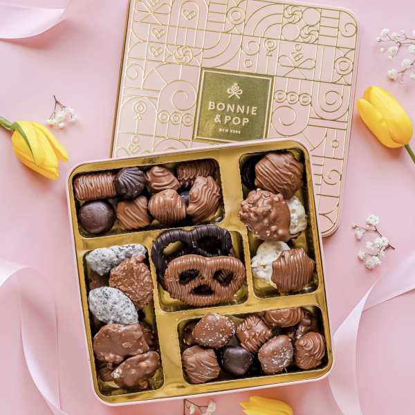 Box of assorted chocolates with yellow tulips on a pink background
