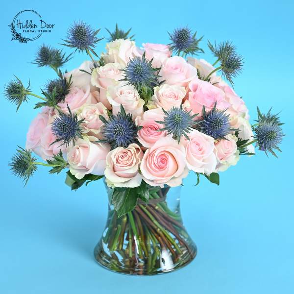 Pink roses in a glass vase with blue thistle flowers