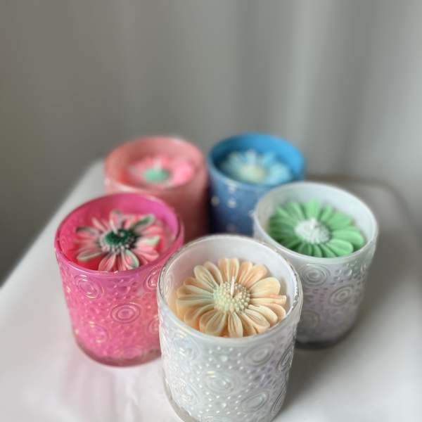 Five flower-shaped candles in colored glass holders on a table