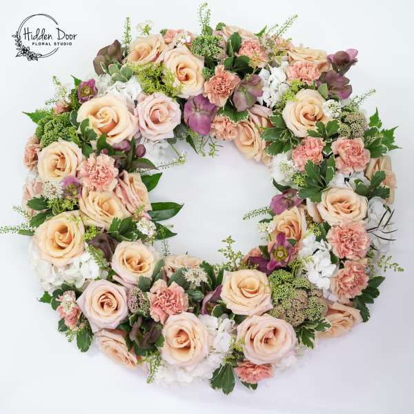 Round floral wreath of peach roses, pink carnations, and white blooms