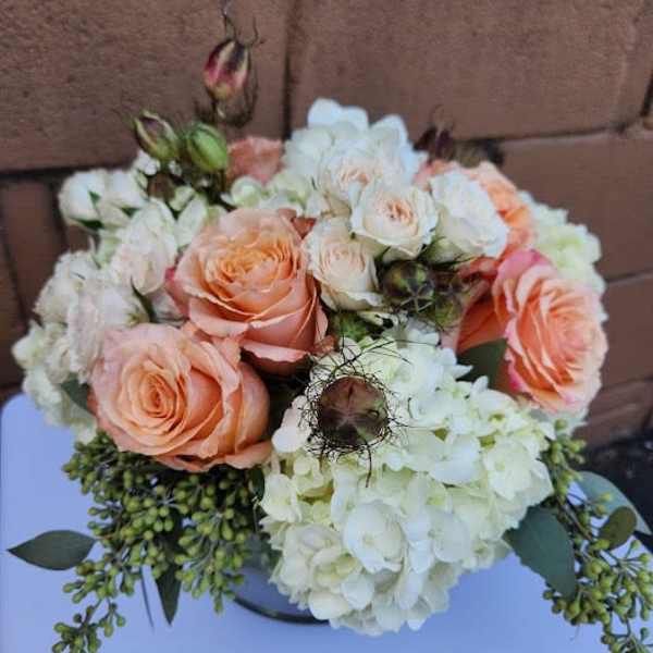 Low arrangement of peach roses and white hydrangeas in a round vase