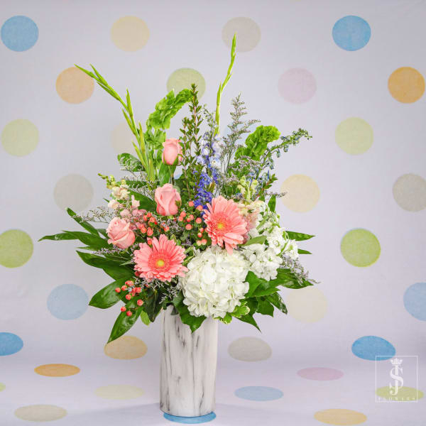 Pink gerberas and roses in a white vase with white hydrangea and tall greenery