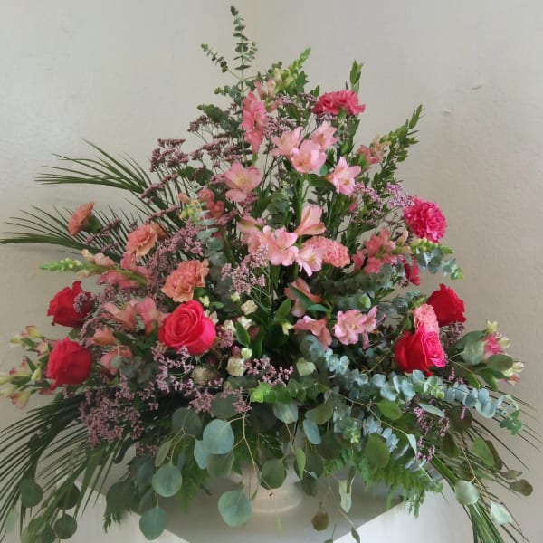 Large pink and red floral arrangement in a white vase