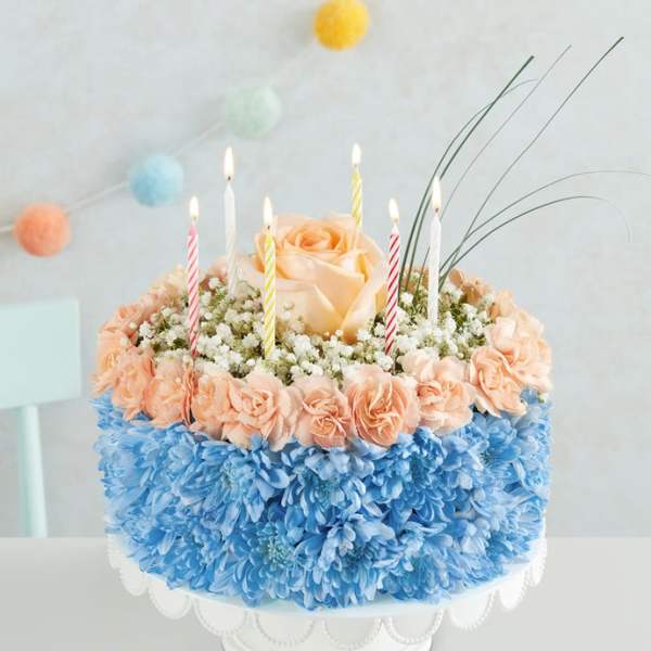 Round floral cake with candles and peach roses on a white stand