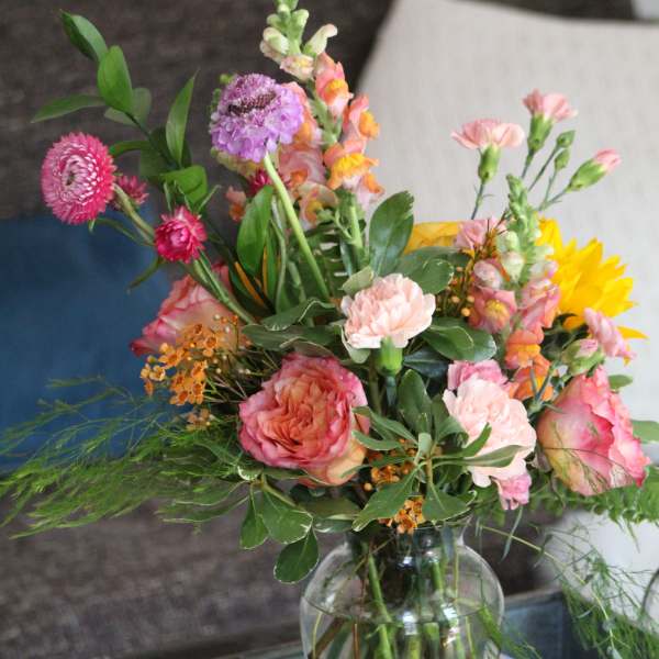 Mixed bouquet of pink, peach, purple, and yellow flowers in a clear glass vase